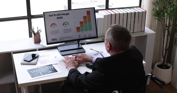 Man in wheelchair diligently analyzing digital business charts and data on a desktop computer, representing an inclusive and accessible work environment for employees with disabilities