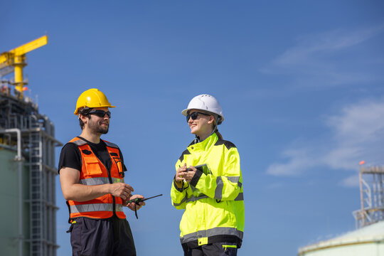 Cheerful engineers discussing LNG terminal project operations at industrial site, Professional team managing liquid natural gas facility safety and production