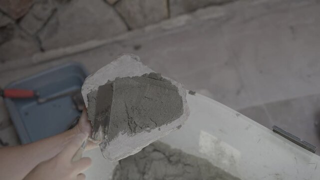 This video shows an overhead view of a worker holding a stone rock veneer upside down and slathering mortar on the back with a trowel.