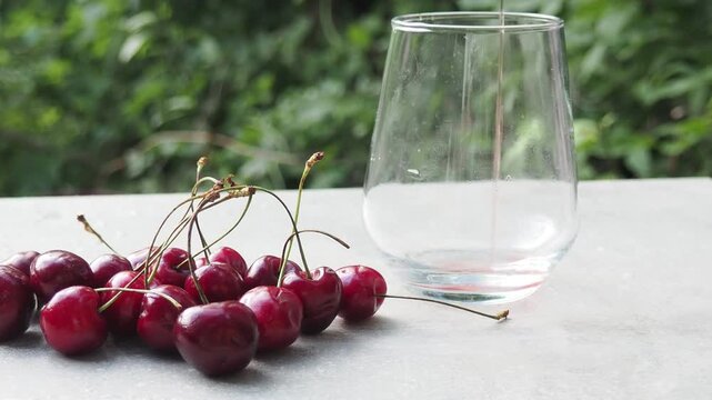 Cold cherry juice in a glass with ripe berries. Delicious cherry juice is poured in a garden against a backdrop of foliage and a cherry tree.
