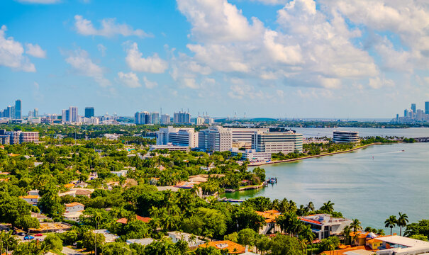  Aerial view of Miami Beach residential neighborhood with Biscayne Bay and downtown Miami skyline in the background Aerial drone photograph capturing a lush, tree-lined residential neighborhood 