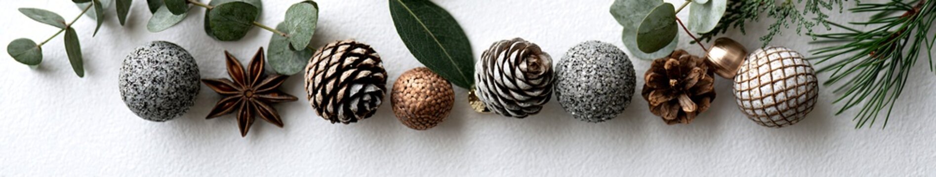 Minimal rustic holiday flat lay with pine cones, textured ornaments, eucalyptus and pine sprigs on white textured background