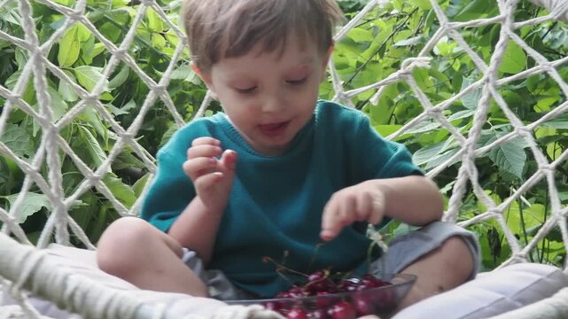 Cherry in kids mouth. Cherry fot kids. Happy kid eating ripe, sweet, juicy, fresh cherries. Child holding cherries. Concept of healthy summer food.
