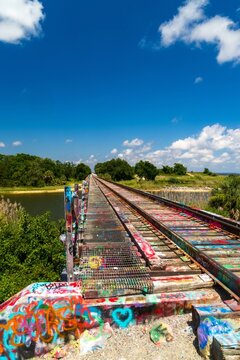 Graffiti covered railroad trestle bridge over river under blue sky