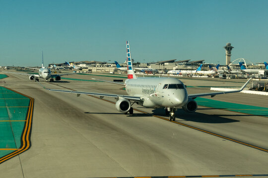 LAX, California, USA - January 7, 2024 - American Eagle Embraer E175 regional jet taxiing head-on at Los Angeles International Airport with United Airlines aircraft, the LAX Theme Building, ATC