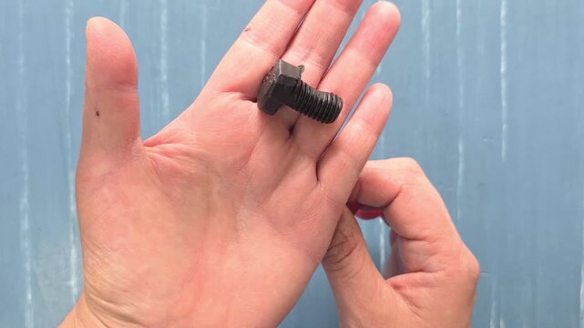 hand holding a screw, Person showing a defective screw with a manufacturing fault.