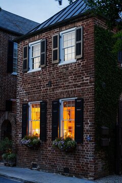 Historic brick townhouse with glowing windows at dusk, Charleston