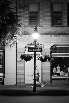 Pedestrian walking past lit lamppost on historic street at night