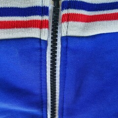 Macro close-up of a black zipper on a blue and white sportswear jacket with red and blue striped collar. © MissExodia