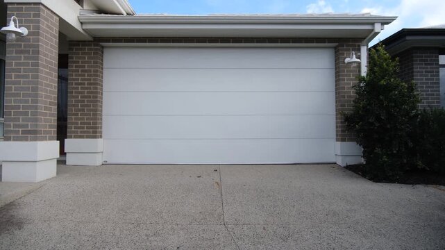 A sectional garage door with a paved driveway fronts a brick veneer home. The standard architectural features of new-build suburban homes in Australia.