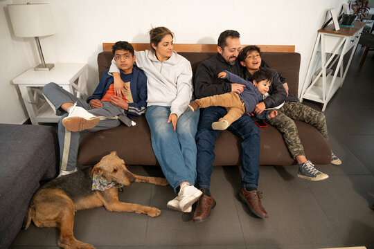 Playful Hispanic family laughing and tickling baby boy on the couch.