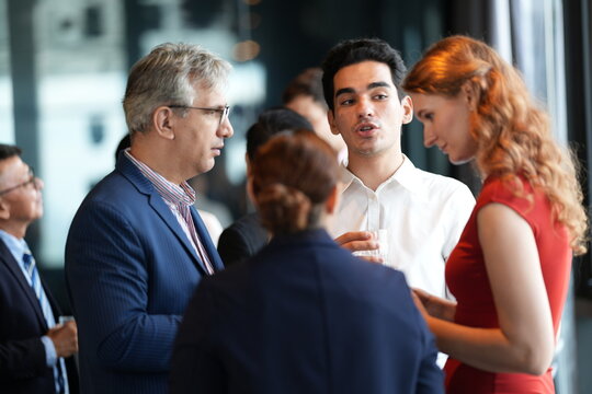 Guests with drinks at a hotel event, mingling and laughing at the reception at a bright hotel reception by the windows, in a stylish contemporary hospitality setting.