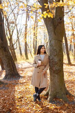 Young woman standing near tree and holding a cup of coffee