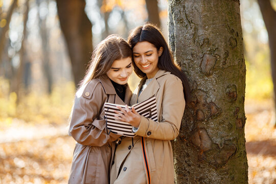 Two girls standing with a book near tree in autumn park