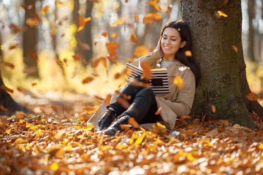 Young woman sitting near tree and reading a book
