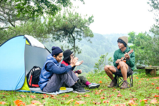 Young Man Playing Ukulele for His Friends While Sitting Outside Their Tent