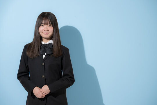 水色背景で制服で立つカメラ目線笑顔の女子中学生や高校生のイメージ