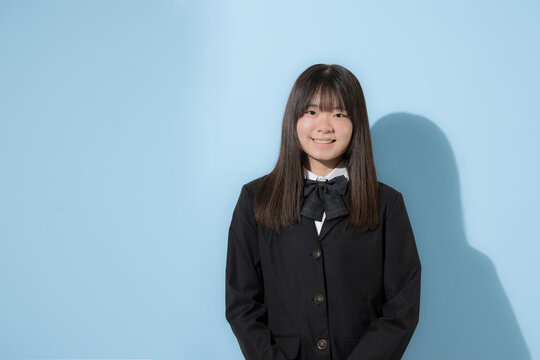 水色背景で制服で立つカメラ目線笑顔の女子中学生や高校生のイメージ