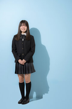 水色背景で制服で立つカメラ目線笑顔の女子中学生や高校生のイメージ正面の全身