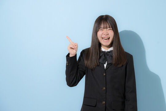 水色背景で制服で立つカメラ目線笑顔の女子中学生や高校生のイメージ　指差しでポイントのポーズで大笑い