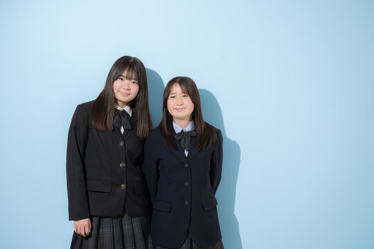 水色背景で本人女子高生や中学生の全身　2人でカメラ目線笑顔の上半身　受験や青春、合格やオープンキャンパスイメージ　右にコピースペースあり
