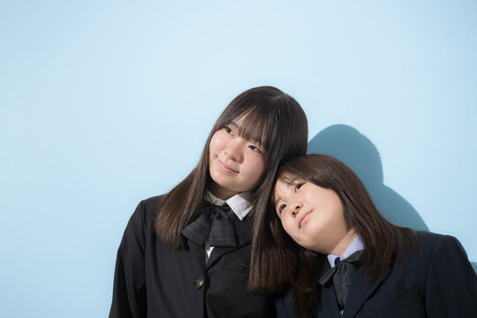 水色背景で本人女子高生や中学生2人で　仲良しで寄り添う友情や友達、仲間や親友イメージ