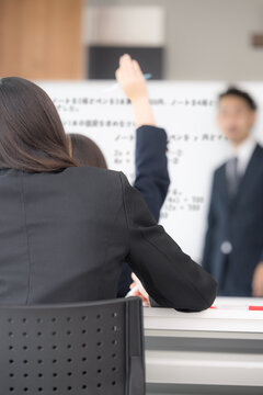 黒板を見ながら、塾や授業で手を挙げる中学生、女高校生と教師の学校の教室での様子　顔無しの後姿