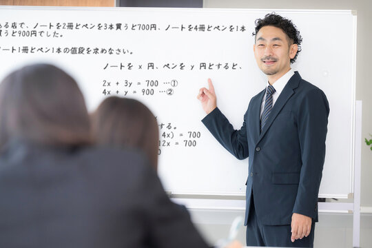 黒板を見ながら、塾や授業で手を挙げる中学生、女高校生と教師の学校の教室での様子