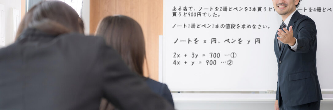 黒板を見ながら、塾や授業で手を挙げる中学生、女高校生と教師の学校の教室での様子　顔無しの後姿のバナー