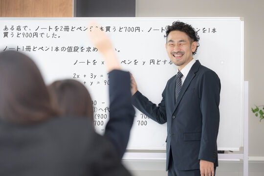 黒板を見ながら、塾や授業で手を挙げる中学生、女高校生の後姿と教師の学校の教室での様子