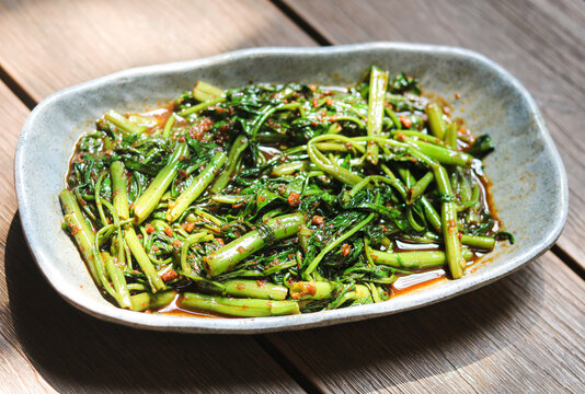 A serving of Stir-Fried Water Spinach with Shrimp Paste (Kangkung Belacan). Captured with natural light on a wooden surface.