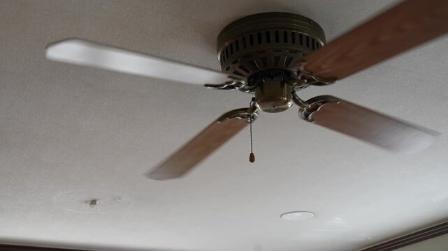 Low angle shot of a wooden ceiling fan spinning slowly in a room