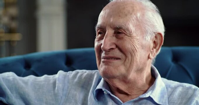 Happy senior man smiling and talking while sitting on sofa at home