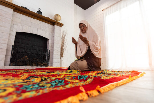 Muslim woman praying for Allah muslim god at room near window. Hands of muslim woman on the carpet praying in traditional wearing clothes, Woman in Hijab, Carpet of Kaaba. Concept of religion Islam