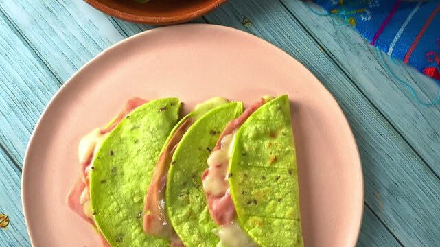 Mexican quesadillas made with green nopal (cactus) tortillas, ham, and melted cheese on a pink plate