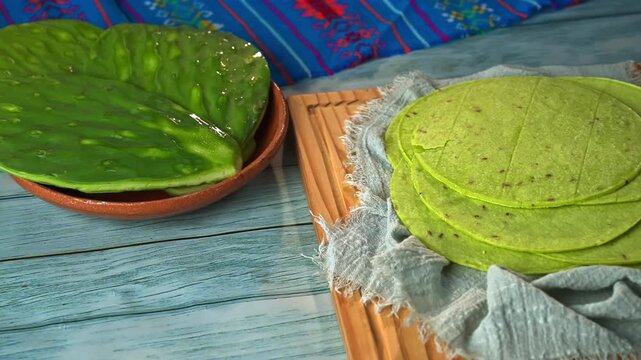 Stack of authentic Mexican green tortillas made with nopal cactus, placed on a wooden cutting board with a rustic cloth and fresh nopales in the background. Healthy and gluten-free food concept