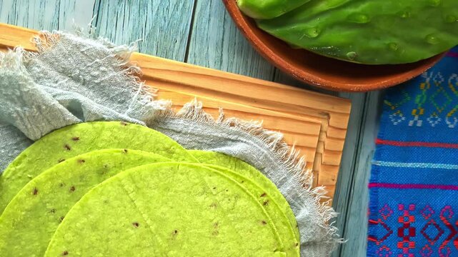 Overhead view of fresh Green Nopal Tortillas with Raw Cactus Paddles on Wooden Board