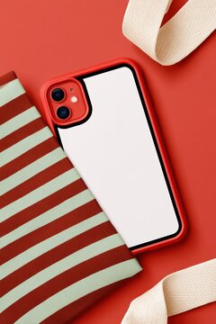 Top-down close-up of an iPhone in a red case beside a striped tote bag and canvas strap