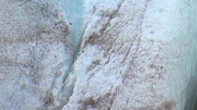 Glimpse the majestic Arctic glacier, its vibrant blue ice interwoven with dark earthy streaks. A pristine icy wall rises above a stony, rugged ground in the frozen northern realm.