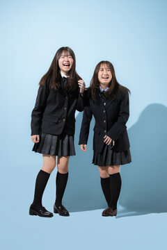 水色背景で躍動感のある大笑いの日本人女子高生や中学生　2人で前向きに進む成長や受験や青春、嬉しいや楽しいハッピーなイメージの全身の正面