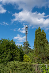 Wysoka antena transmisyjna w obszarze podmiejskim otoczona pojedynczymi drzewkami na tle błękitnego nieba z małą ilością chmur w zachodniej Polsce w porze letniej  © mbugajsky
