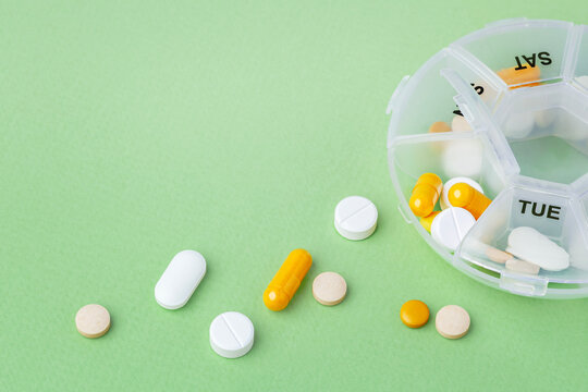 Vitamins and supplements with daily pill box on green background
