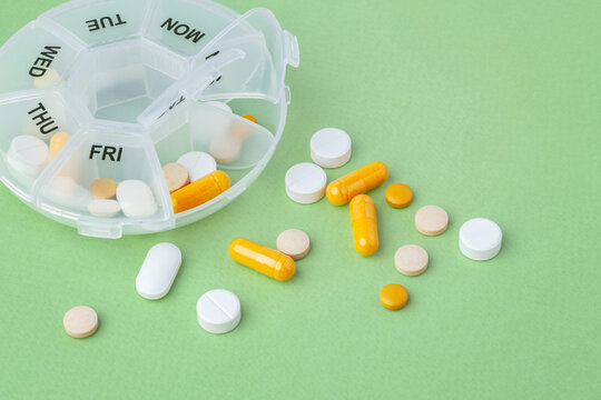 Capsule, pills and supplements with pill box organizer on green background