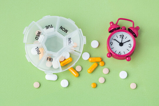 Pill box organizer with medication and alarm clock on green background