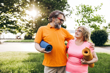Naklejka premium Happy seniors holding yoga mats standing in park