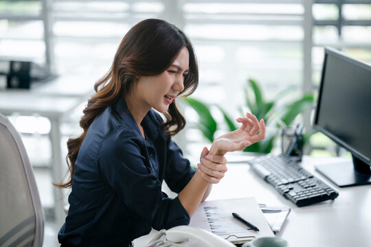 Woman holds hand in pain while working, office syndrome
