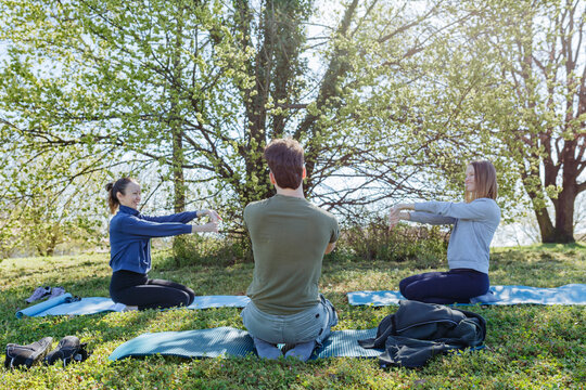 Three Friends Practicing Outdoor Stretching on Yoga Mats in a Sunny Park