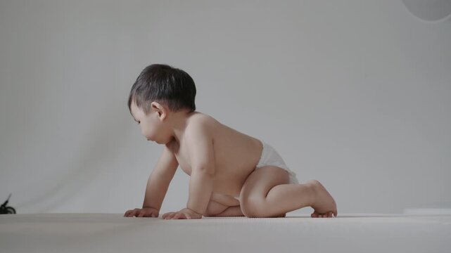Adorable infant wearing diaper sitting on mat in bright room, growth concept.