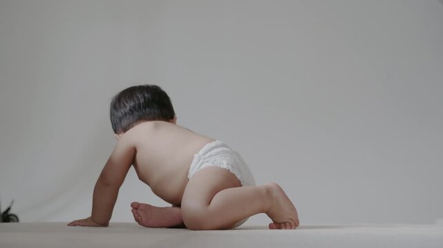 Adorable infant wearing diaper sitting on mat in bright room, growth concept.