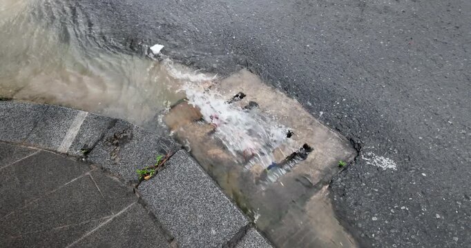 Slow motion video of a concrete storm drain clogged with debris and trash during heavy rain.